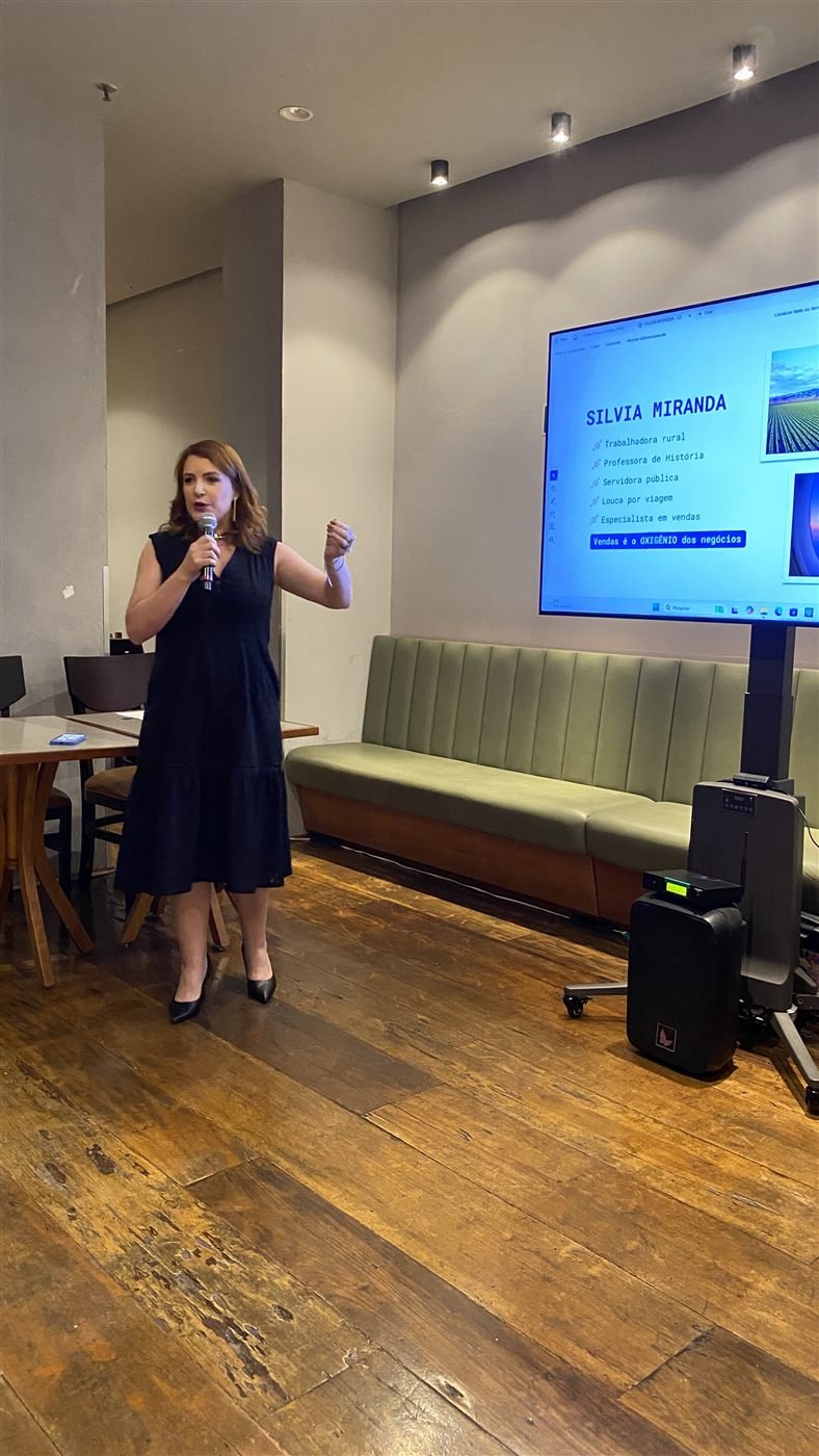 Silvia Miranda palestrando no Clube Dellas, com slide de apresentação ao fundo